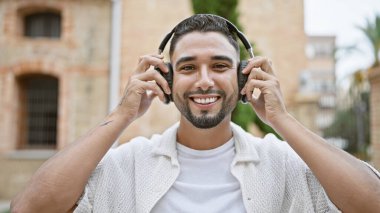Sakallı yakışıklı genç bir adam şehir sokaklarında kulaklıkla müzik dinliyor..