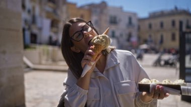 Genç bir İspanyol kadın güneşli bir günde, Bari, İtalya 'nın eski caddelerinde büyük bir dondurma külahının tadını çıkarıyor..