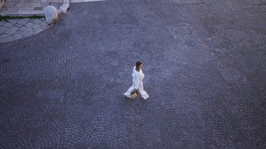 Beyaz elbiseli genç bir İspanyol kadın, Bari, İtalya, Puglia 'daki eski kasabanın kaldırım taşlı sokaklarında yürür. Şehir merkezinden yakalanır..