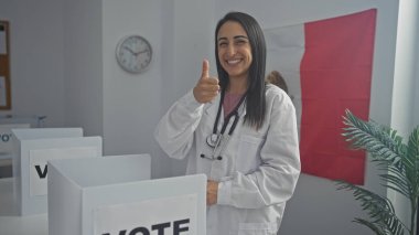 Gülümseyen kadın doktor arka planda Meksika bayrağı olan bir oy kabininde başparmak kaldırıyor..