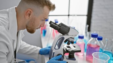 Laboratuvarda mikroskop kullanan odaklanmış bir adam. Etrafı bilimsel ekipmanlarla çevrili..