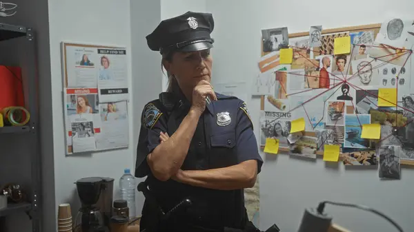 stock image A thoughtful female police officer ponders a case in a detective's office lined with investigation evidence and missing person posters.