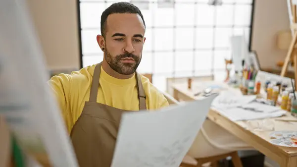 stock image A focused man holding paper in an art studio examines his work with a contemplative expression.