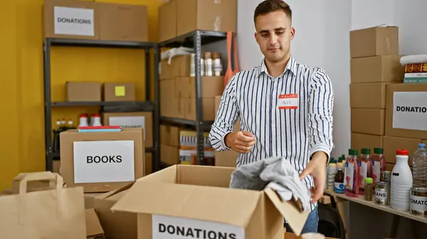 stock image A young man organizes donated items in a warehouse with boxes labeled 'books' and 'donations'.