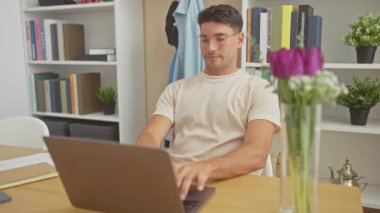 Neşeli, genç, İspanyol bir adam evinde dizüstü bilgisayarıyla çalışırken rahatlık ve verimliliği resmediyor..