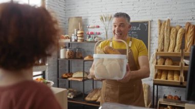 Gülümseyen fırıncı modern fırında kadına arka planda fırınlanmış ürünlerle ekmek sepeti sunuyor.