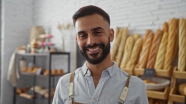 Fırında gülümseyen sakallı yakışıklı adam. İçi ekmek raflarıyla dolu.