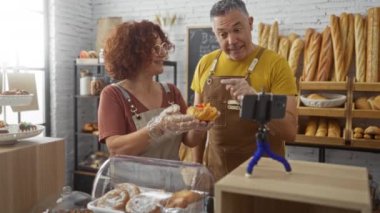 Erkek ve kadın fırında birlikte video çekiyorlar, fırın ürünlerini ev ortamında coşkuyla sergiliyorlar.