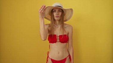 Bikinili bir kadın yaz şapkalı, izole edilmiş sarı arka planda kendine güvenen İtalyan jestleri yapıyor.