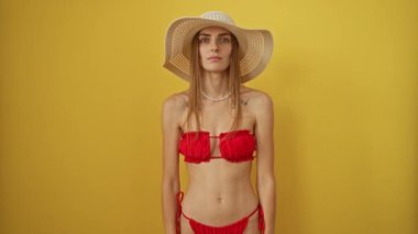 Bikini giyen, şapkalı, sessiz dudaklı bir kadın. Kafkas güzelliği, izole edilmiş sarı arka planda gizli bir jest sergiliyor.