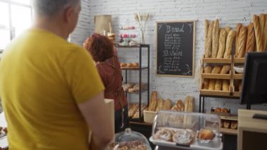 Kadın fırın tezgahındaki adama ekmek ve hamur işleri sunuyor.