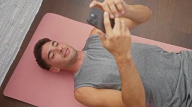 İçerideki yoga minderinde uzanmış gülümseyen genç adam akıllı telefonuyla selfie çekiyor.