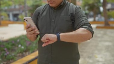 İspanyol adam, şehir parkında telefon tutarken akıllı adamı kontrol ediyor.