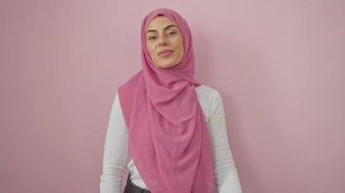 Tesettürlü neşeli, genç bir İspanyol kadın, kollarını kavuşturmuş, kameraya ışıltılı bir gülümseme gösteriyor. Pembe izole arkaplanda mükemmel bir ekran görüntüsü.