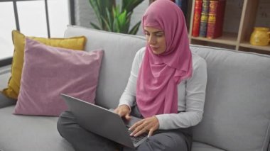 Başörtüsü takan genç bir İspanyol kadın evde dizüstü bilgisayarda çalışıyor, şaşırdığını ve güvensizliğini dile getiriyor..