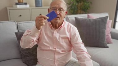 Evindeki dekore edilmiş oturma odasında minderlerle çevrili rahat bir koltukta otururken kredi kartı tutan yaşlı bir adam..