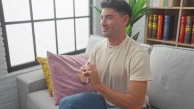 Rahatlamış genç İspanyol bir adam. İçerideki kanepede uzanıyor. Mutlu bir gülümsemeyle..