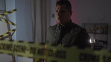 Latin kökenli bir adam, dikkat bandıyla loş bir şekilde aydınlatılmış cinayet mahalline silah doğrultuyor, gerilim yaratıyor..