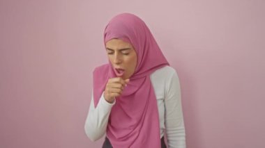 Hasta, tesettürlü, pembe arka planda öksüren, soğuk algınlığı veya bronşit belirtilerini gösteren genç İspanyol bir kadın. sağlık hizmeti kavramı.