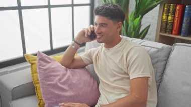 Yakışıklı, İspanyol asıllı, akıllı telefonda gülen, evdeki kanepede oturan..