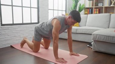 İspanyol adam modern oturma odasında konfor ve konsantrasyonla pembe paspas üzerinde egzersiz yapıyor.