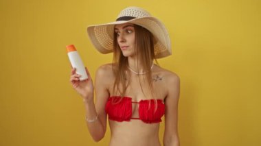 Bikinili kadın elinde güneş kremi tutuyordu ağzı şok olmuş bir ifadeyle, sarı arka planda izole edilmiş, şaşırmış ve korkmuştu.