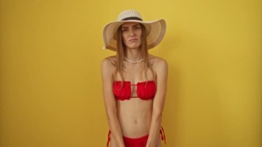 Sarı bikinili ve yaz şapkalı kadın üzgün ve üzgün görünüyor. Sarı arka plan karşısında endişeli bir ifade takınıyor. Stres ve endişe yüzünden ağlıyor.