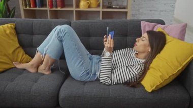Genç bir İspanyol kadın evdeki kanepede uzanmış, kredi kartını incelikle inceliyor..