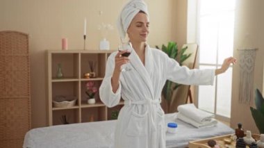 Spa Sağlık Merkezi 'nde bornoz ve havlu giymiş genç bir kadın. Kapalı alanda dans ederken elinde şarap kadehi tutuyor.