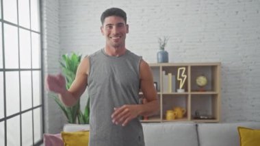 Atletik kıyafetli neşeli bir İspanyol adam şık bir oturma odasında güven içinde poz veriyor..