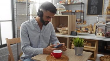 Kulaklık takan genç adam sıcak bir fırında otururken akıllı telefon kullanıyor..