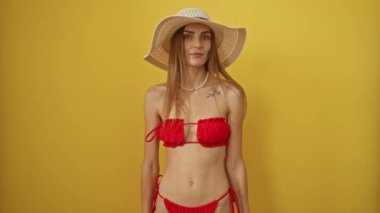 Yazlık şapkalı ve bikinili bir kadın, aşk ifadesiyle öpüşüyor, genç ve güzel beyaz, seksi ve neşeli görünüyor, sarı arka planda soyutlanmış.