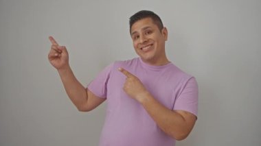 Genç, İspanyol bir adam beyaz bir arka planda tek başına duruyor, iki eliyle kameraya bakıp gülümserken neşeyle yüzünü gösteriyor..