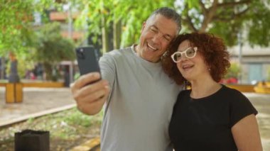 Şehir parkında bir video görüşmesi sırasında gülümseyen mutlu orta yaşlı çift..