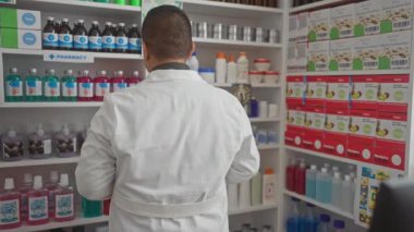 Modern eczanede beyaz önlüklü, ilaç raflarıyla gülümseyen İspanyol erkek eczacı..