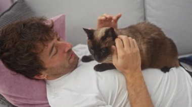 Rahat bir adam, sıcak bir oturma odasında kanepede siyam kedisiyle vakit geçirmekten zevk alır..