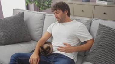 Karnı ağrıyan genç bir İspanyol adam oturma odasındaki kanepede kucağında bir kedi yavrusuyla oturuyor.