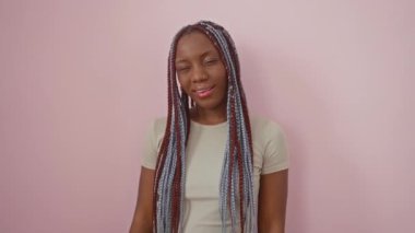 Neşeli Afrikalı Amerikalı kadın, kameraya neşeyle göz kırpıyor, doğal ışıkta seksi bir göz kırpma. Pembe soyutlanmış arka plana karşı durmak, neşeli bir yüz ifadesi sergilemek,.