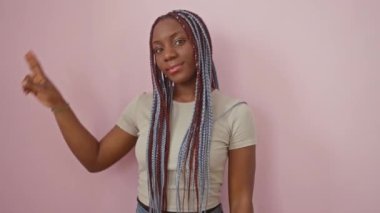 Neşeli Afro-Amerikalı kadın izole edilmiş pembe bir duvara karşı duruyor, neşe dolu bir zafer işareti gösteriyor, olumlu gülümsüyor ve doğrudan kameraya bakıyor.
