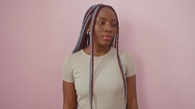 Neşeli Afro-Amerikalı kadın, pembe bir arka planda dikilirken güzel bir şekilde gülümsüyor, eliyle bir telefon görüşmesi yapıyor..