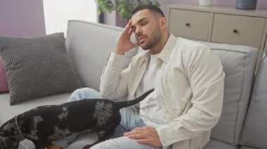 Genç İspanyol bir adam modern bir apartman dairesinde tekel köpeğiyle rahatlıyor, rahat ve şehir tarzı yayıyor..