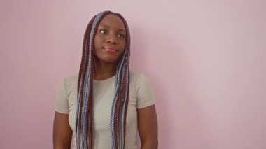 Afro-Amerikalı kadın gülümseyip yan tarafa bakıyor ve düşünüyor. izole edilmiş pembe arkaplan