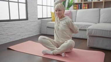Yoga yapan dingin bir kadın modern oturma odası ortamında pembe bir paspasın üzerinde poz veriyor. Huzur ve zindelik simgeliyor..