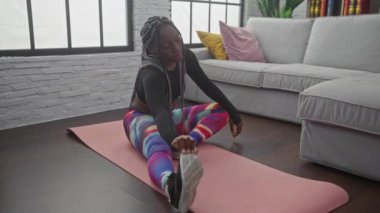 Afrika kökenli Amerikalı bir kadın yoga minderinin üzerinde oturma odasında uzanıyor.