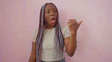 Afallamış Afro-Amerikalı kadın yan tarafı işaret ediyor, ağzı açık ve şaşırıyor. Eğlenceli pembe bir arka planda tek başına duruyor. Gerçekten inanılmaz.!