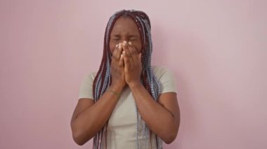 Neşeli Afro-Amerikalı kadın, gülen ağızları eliyle kapatıyor pembe soyutlanmış arka plana karşı duruyor, sulu dedikodu skandalının tadını çıkarıyor, tişört ve saç örgüsü takıyor, mutlu utancı kucaklıyor..