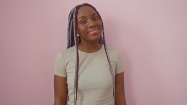 Kendine güvenen Afro-Amerikalı kadın pembe bir arka plana karşı duruyor, pozitif ve başarı saçan serin, mutlu bir gülümseme sergiliyor..