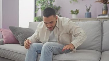 Genç, yakışıklı, İspanyol bir adam oturma odasında rahat bir koltukta oturur. Çiçekler ve yastıklarla..