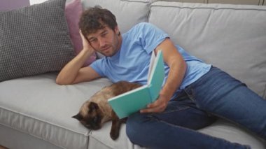 Evde kanepede siyam kedisiyle kitap okuyan sıradan bir adam..