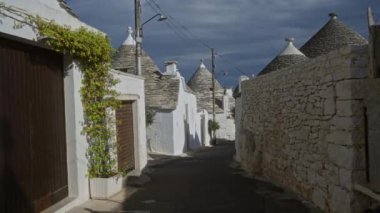 Büyüleyici Alberobello, Puglia, İtalya 'da geleneksel Trulli evleri olan manzaralı bir sokak. Beyaz taş duvarlar, eşsiz konik çatılar ve huzurlu bir açık hava manzarası var..